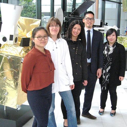 Eine Gruppe Studierender steht vor Satellitenbauteilen.