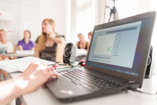 Einblick in praxisorientierte Lehre: Studierende arbeiten an einem computergestützten Stimmfeld und diskutieren.