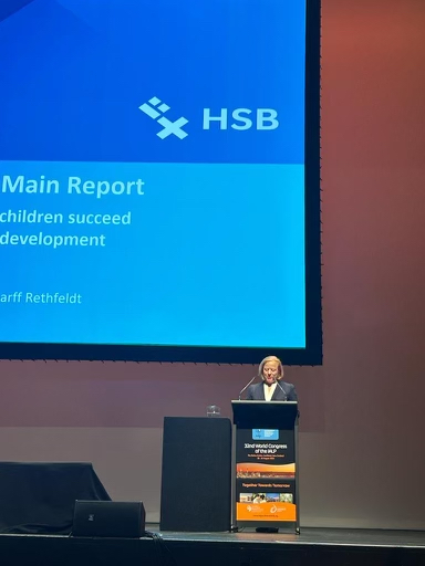 Professorin Scharff Rethfeldt hält einen Vortrag auf einer großen Bühne. Im Hintergrund eine übergroße Folie mit dem Vortragstitel und dem Logo der HSB.